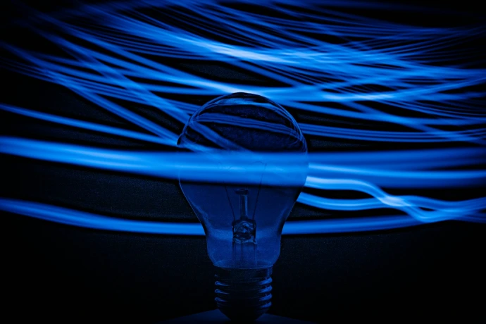 A light bulb surrounded by long exposure blue light trails against a dark background